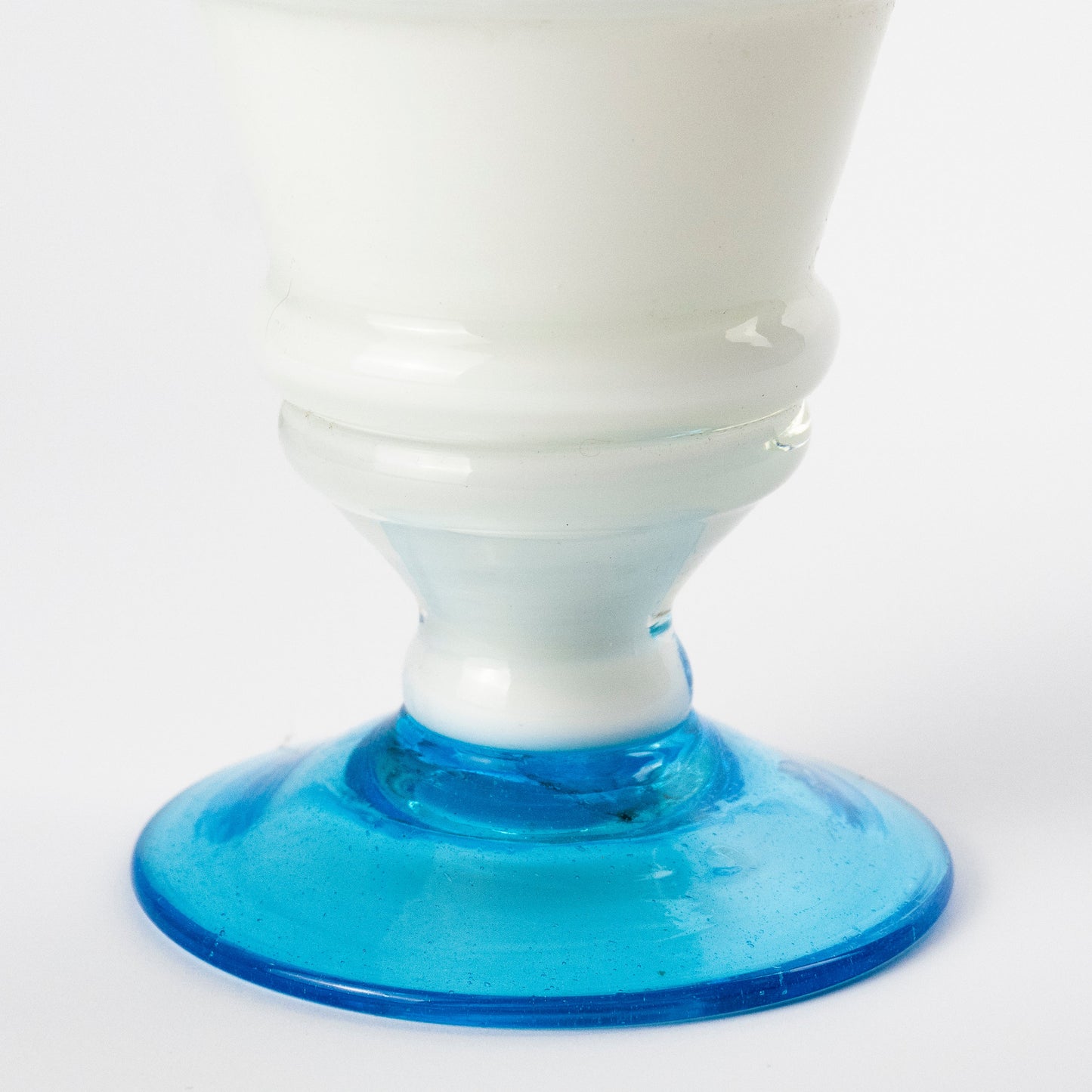 A close-up of a white murano glass pitcher with a flared blue glass base, photographed against a clean white background.