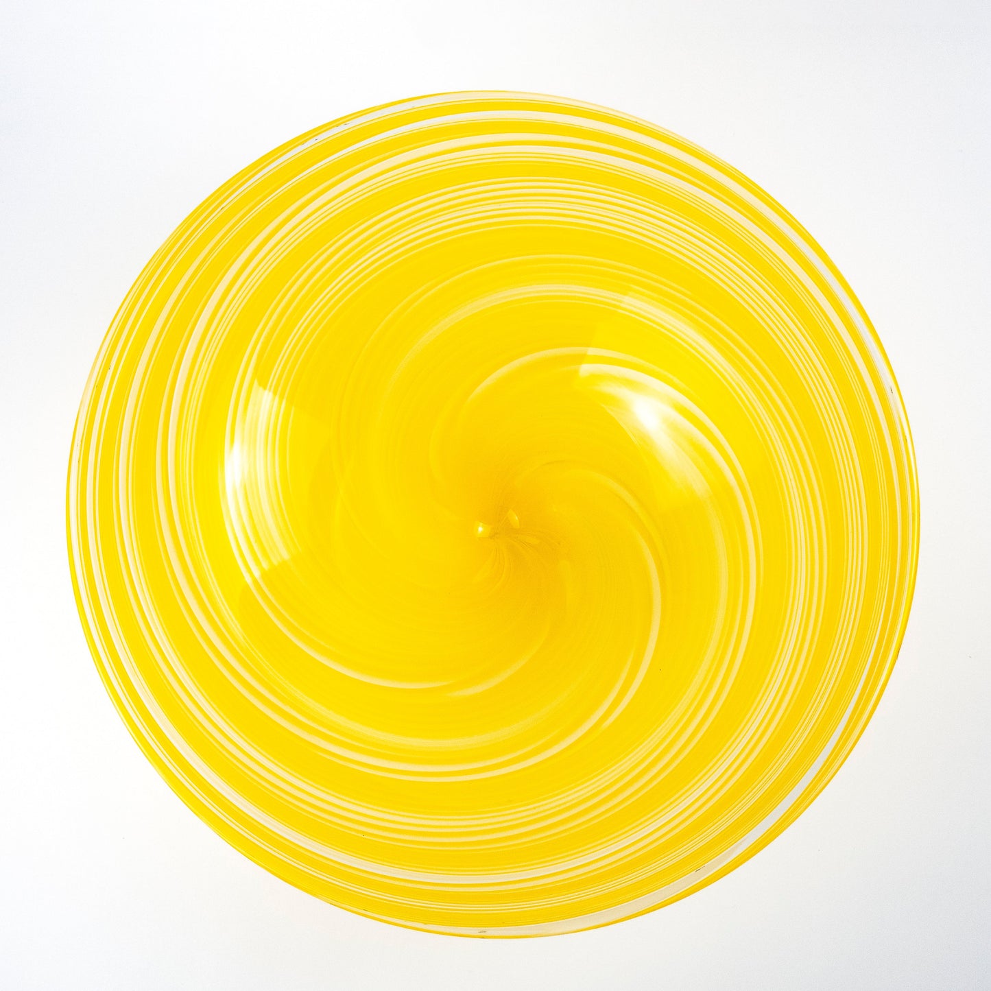 A bright yellow glass bowl with a spiral pattern of concentric rings, photographed from directly above on a white background.