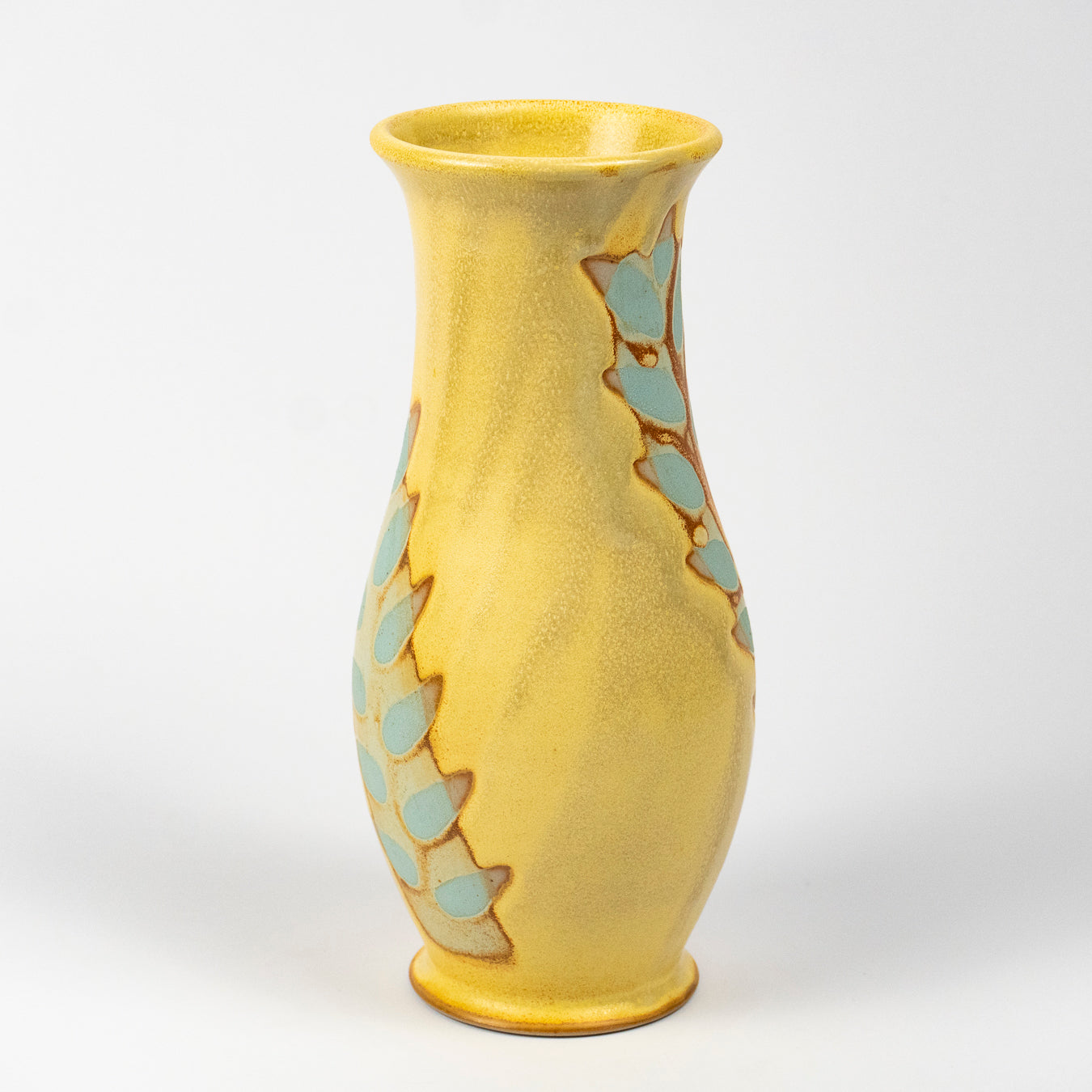 A yellow ceramic vase with a textured glaze, decorated with light blue scalloped leaf patterns outlined in brown, set against a plain light gray background.
