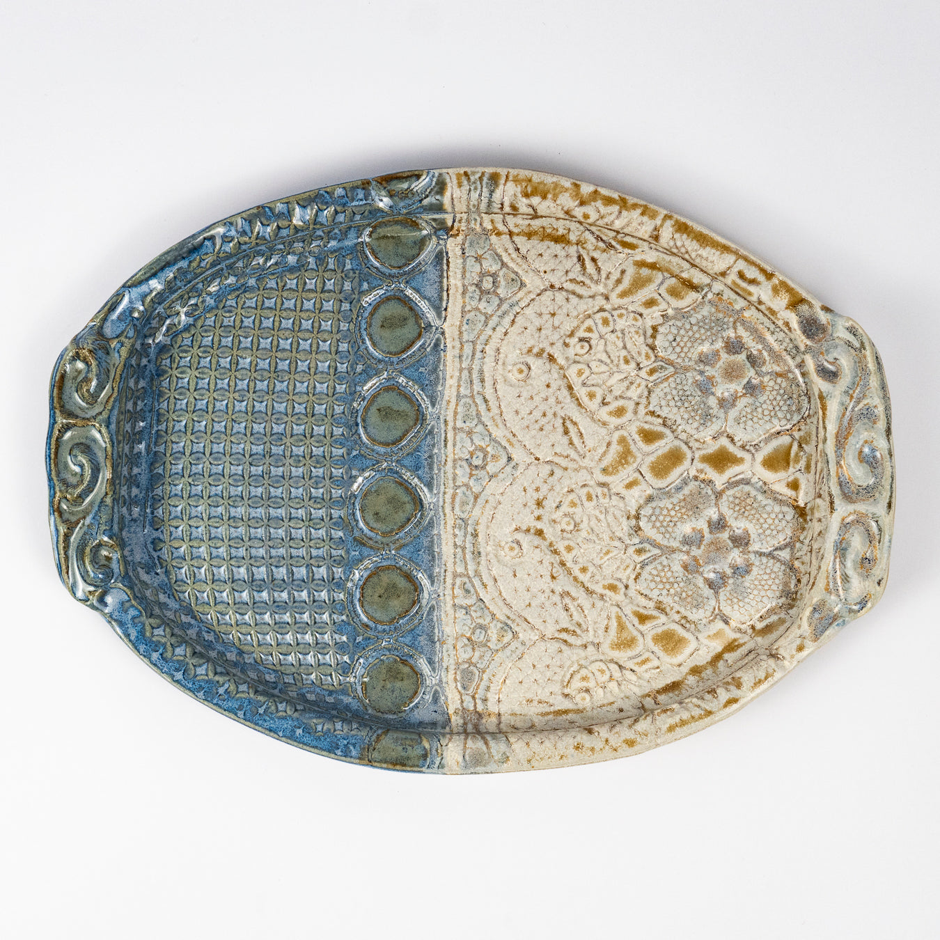 An oval ceramic serving tray with a split design, featuring a textured blue glaze on one half and an embossed beige floral pattern with brown accents on the other, set against a plain white background.