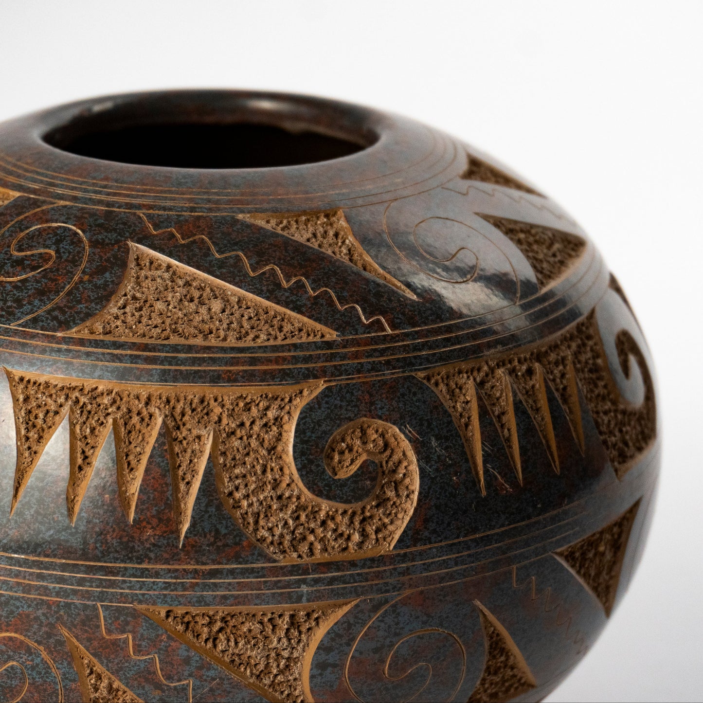 A close-up of a round ceramic pot with a dark brown and black glaze, decorated with geometric and tribal-inspired patterns in a contrasting warm brown.