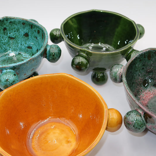 Ballo ceramic bowls in four colorways — teal, green, orange, and pink-green speckle — with sculptural bobble details and ball feet