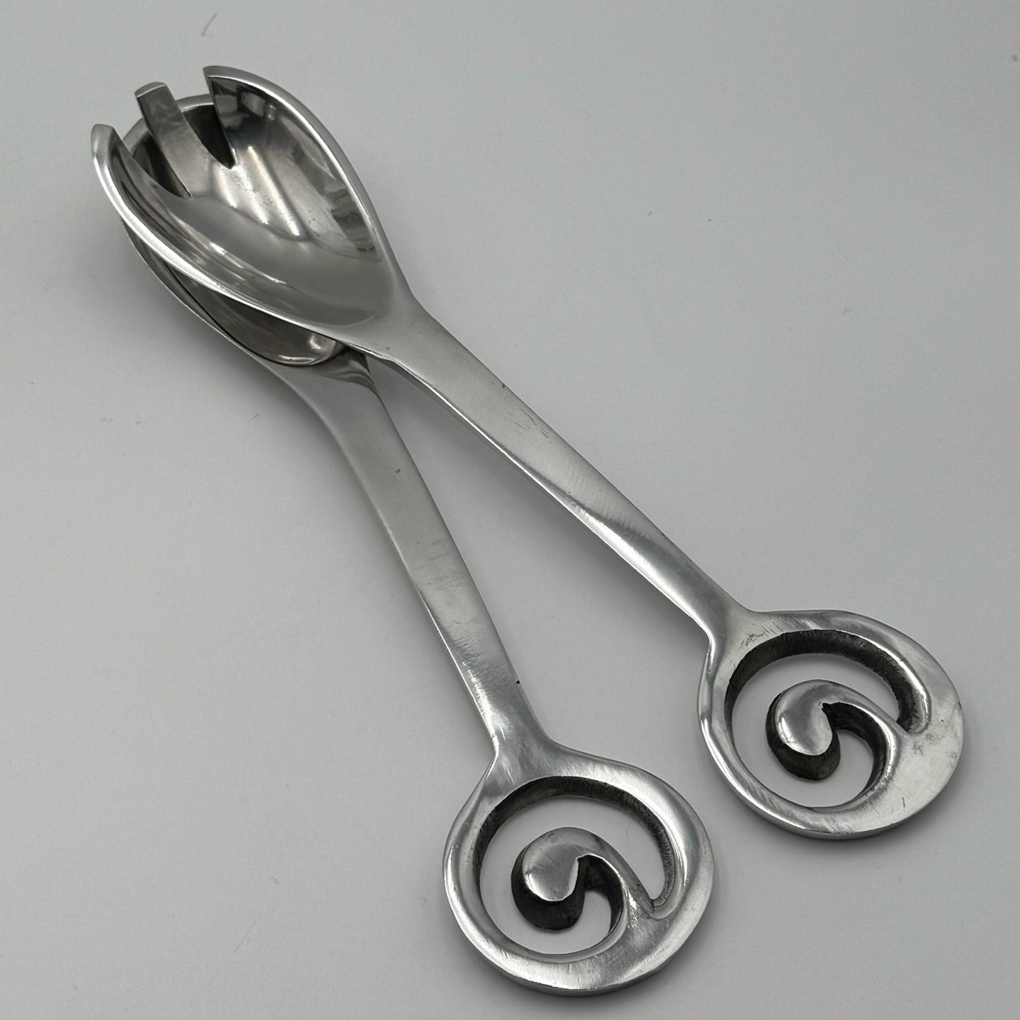 Pair of silver salad servers with decorative handles on a gray background