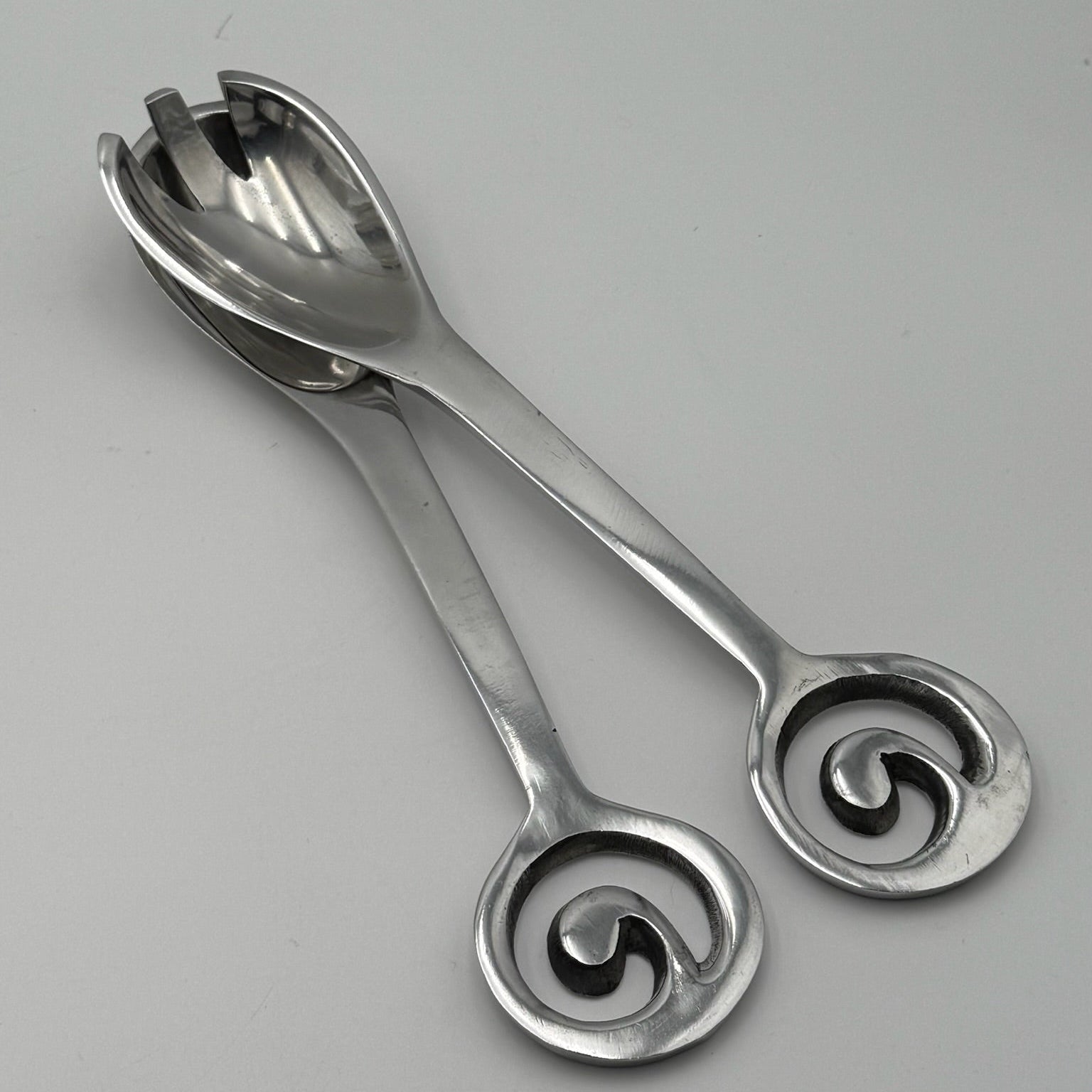 Pair of silver salad servers with decorative handles on a gray background