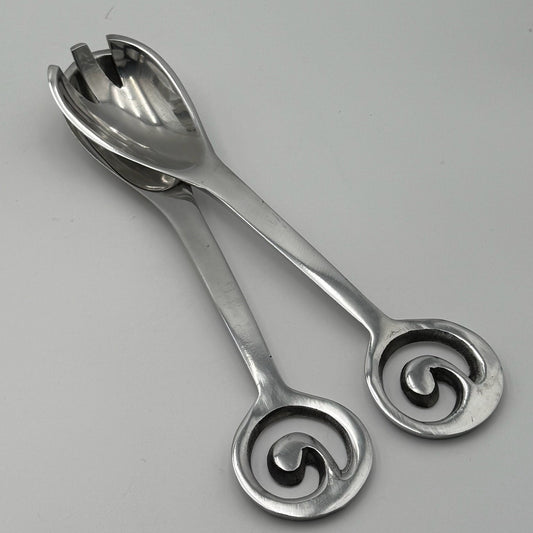 Pair of silver salad servers with decorative handles on a gray background