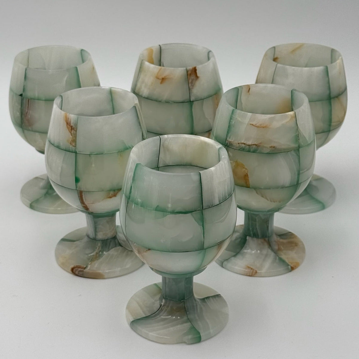 Set of six green and white patterned glass goblets on a white background
