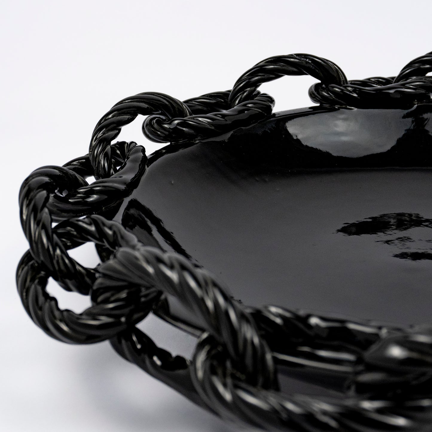 A close up of the Rassilo ceramic round platter, glossy black glaze, openwork twisted rope chain-link rim