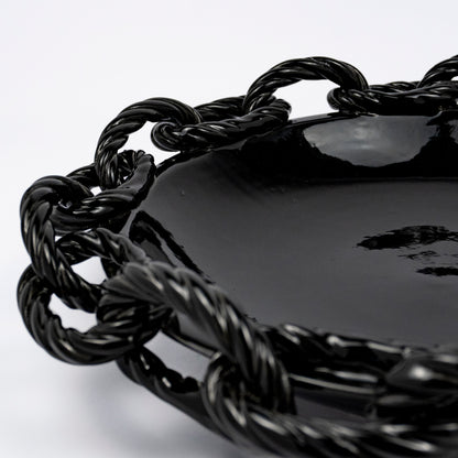 A close up of the Rassilo ceramic round platter, glossy black glaze, openwork twisted rope chain-link rim
