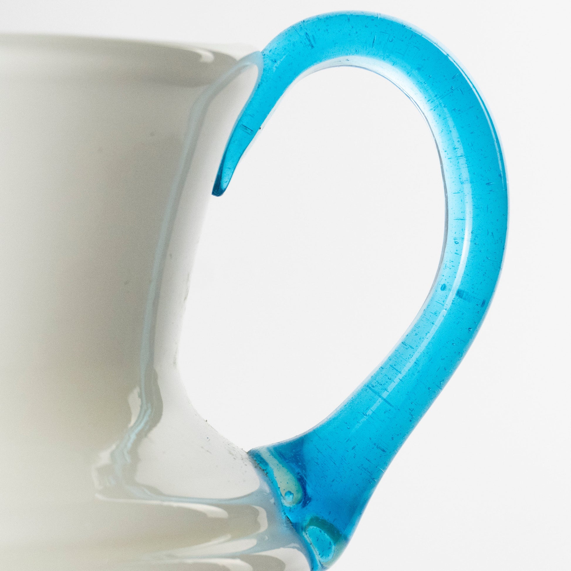 Close-up of a white murano glass pitcher with a vibrant, translucent blue glass handle against a clean white background.