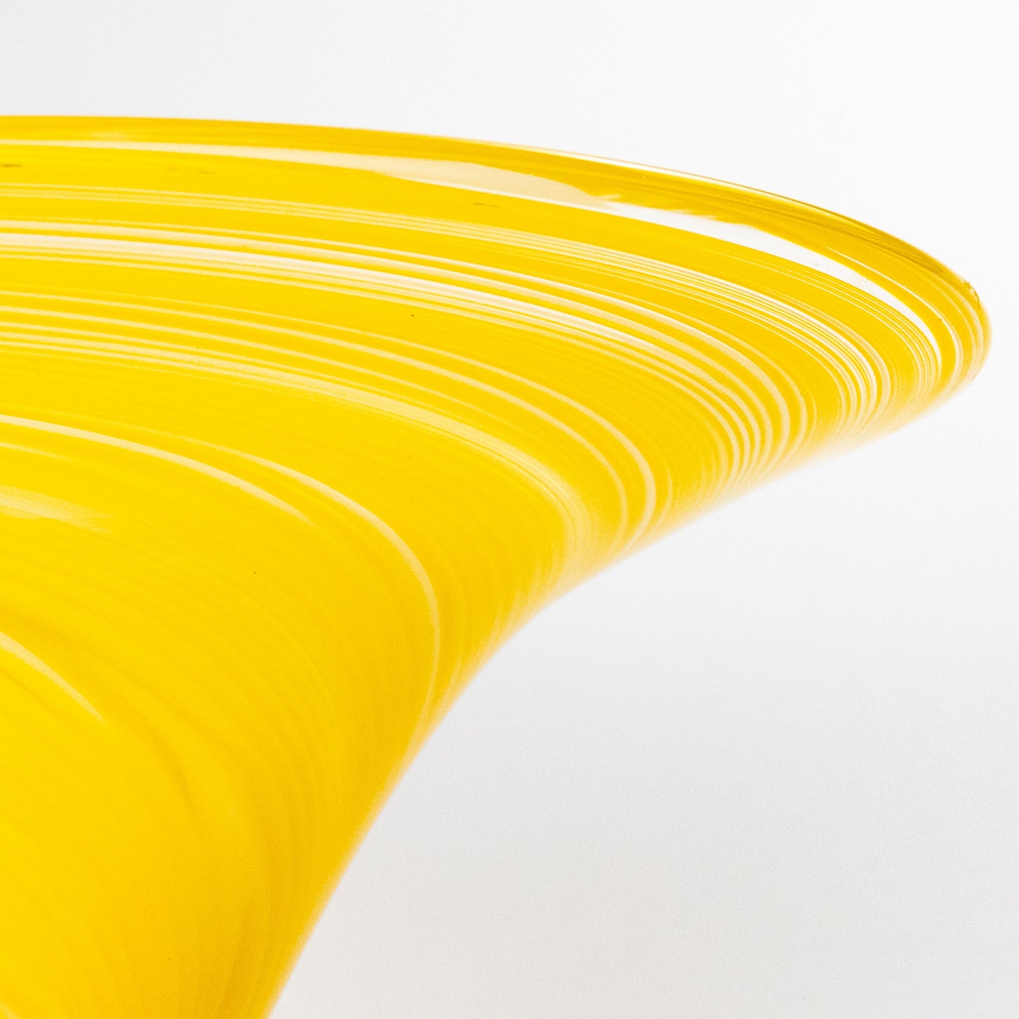 A close-up studio shot of a translucent yellow glass bowl with a flared rim and curved, sculptural form on a white background.