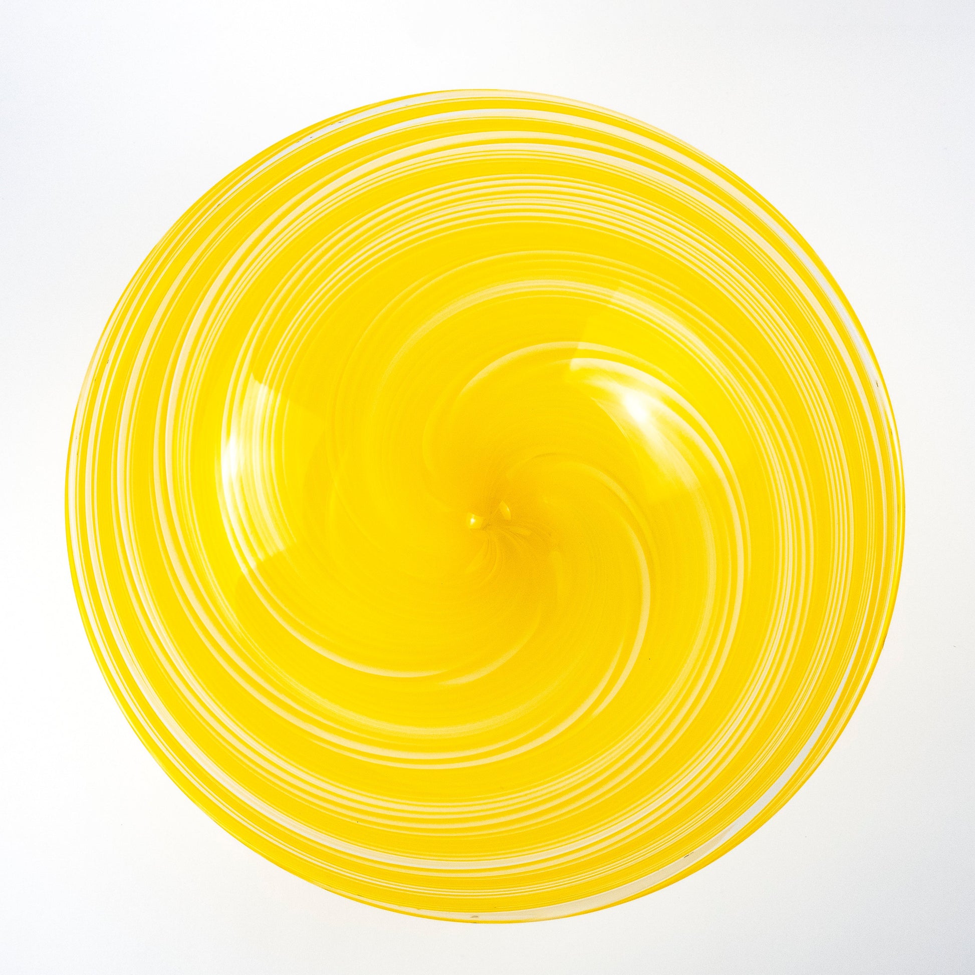A bright yellow glass bowl with a spiral pattern of concentric rings, photographed from directly above on a white background.