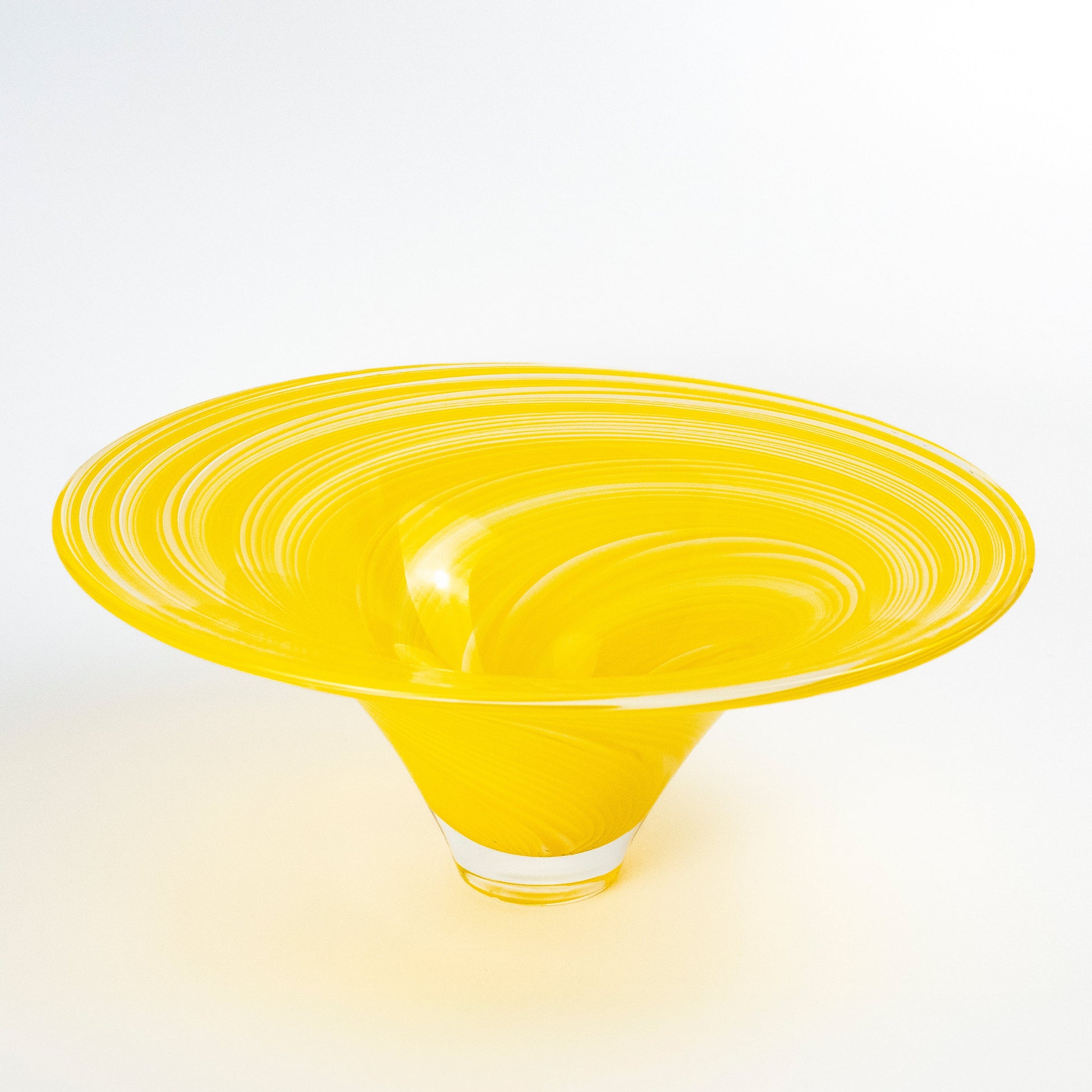 A bright yellow hand-blown glass bowl with concentric swirl patterns on the exterior, set against a clean white background.