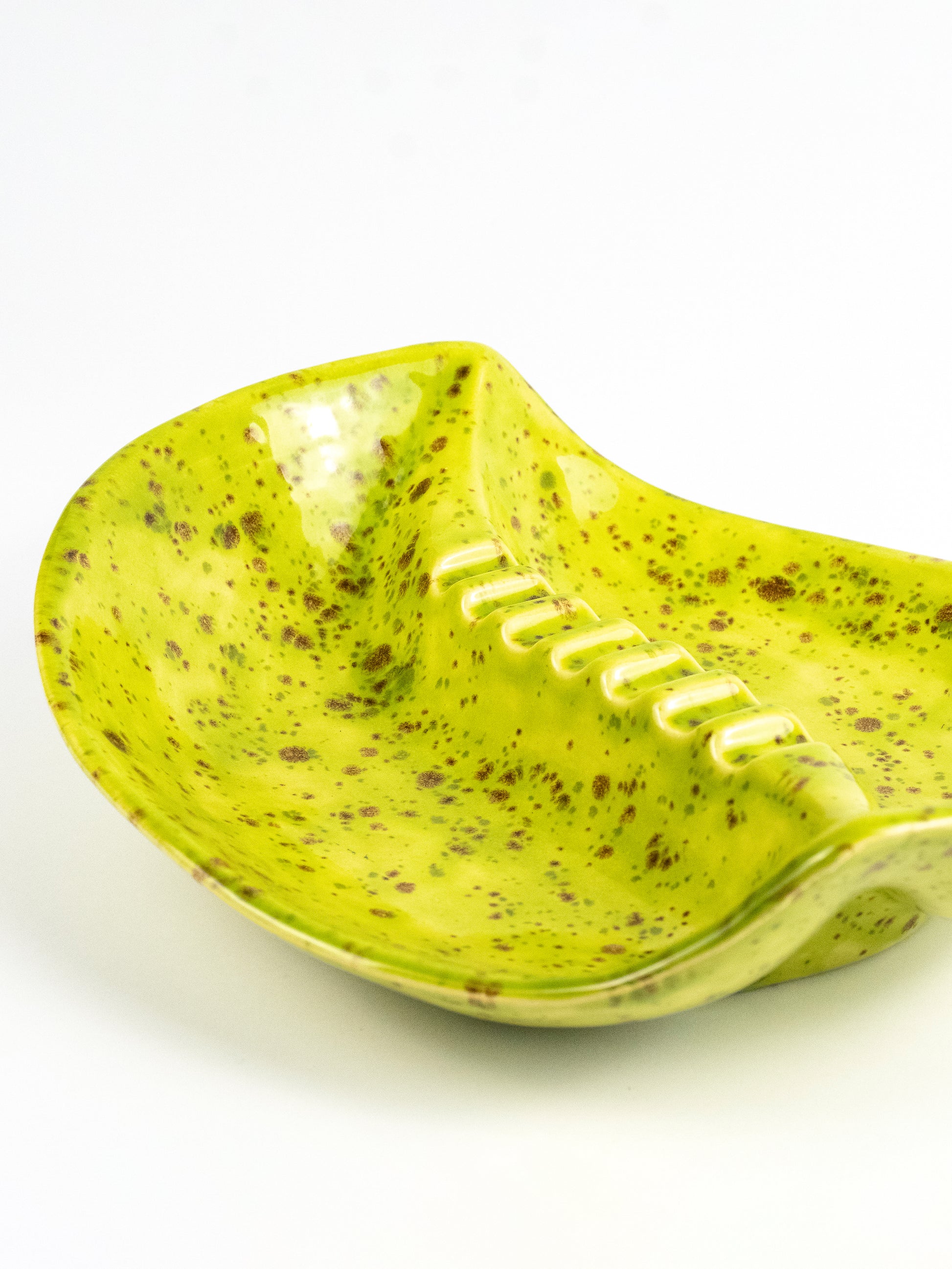 A ceramic bowl with a wavy, spoon-like form, featuring a bright lime green glaze speckled with brown and white spots, set against a plain white background.