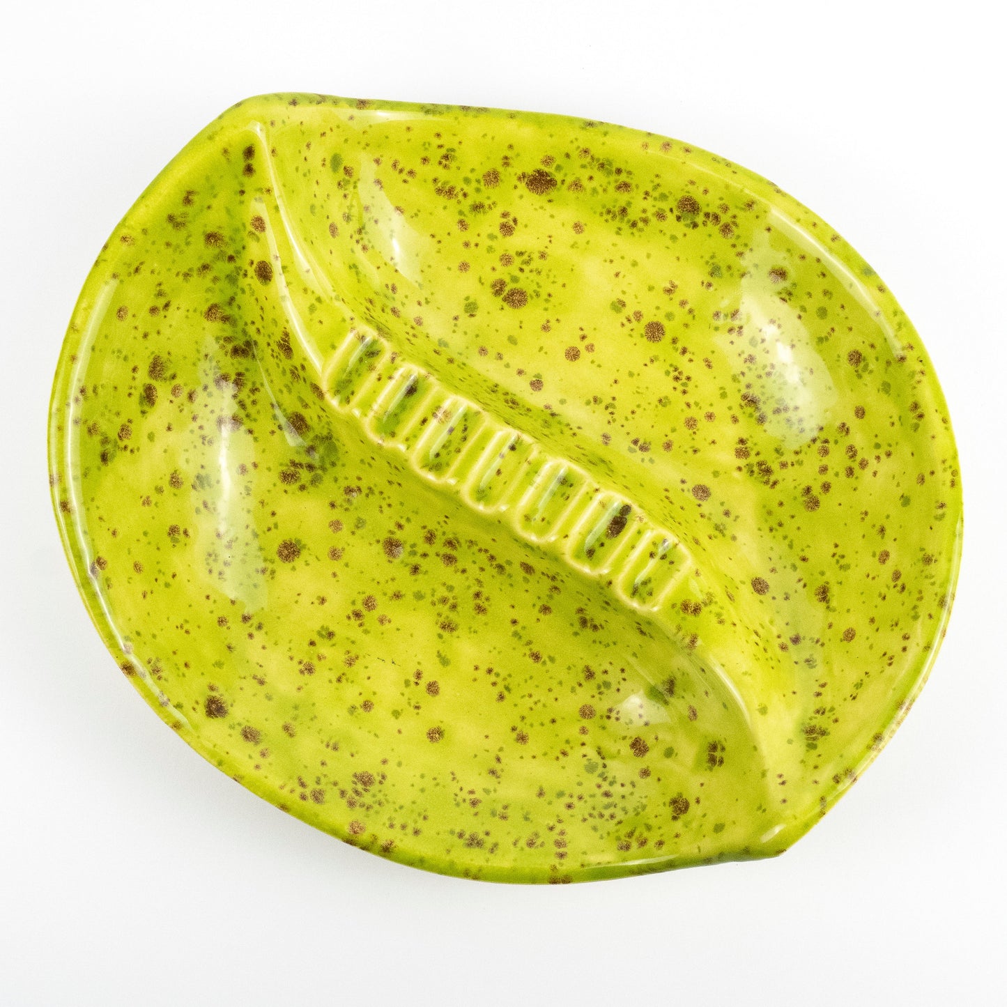 A glossy, leaf-shaped ceramic dish or tray in a bright yellow-green glaze with brown speckles, photographed from directly above on a white background.