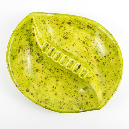 A glossy, leaf-shaped ceramic dish or tray in a bright yellow-green glaze with brown speckles, photographed from directly above on a white background.