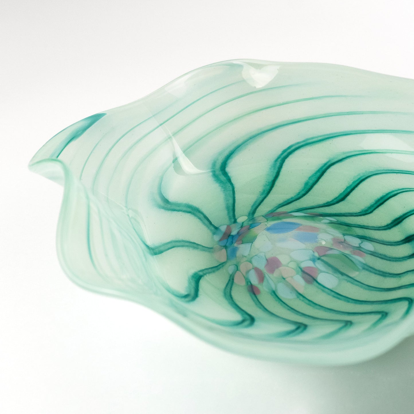 A hand-blown glass bowl with a wavy, organic shape, featuring a translucent pale mint green body with dark green wavy lines and a colorful bubble burst near the center, set against a clean white background.