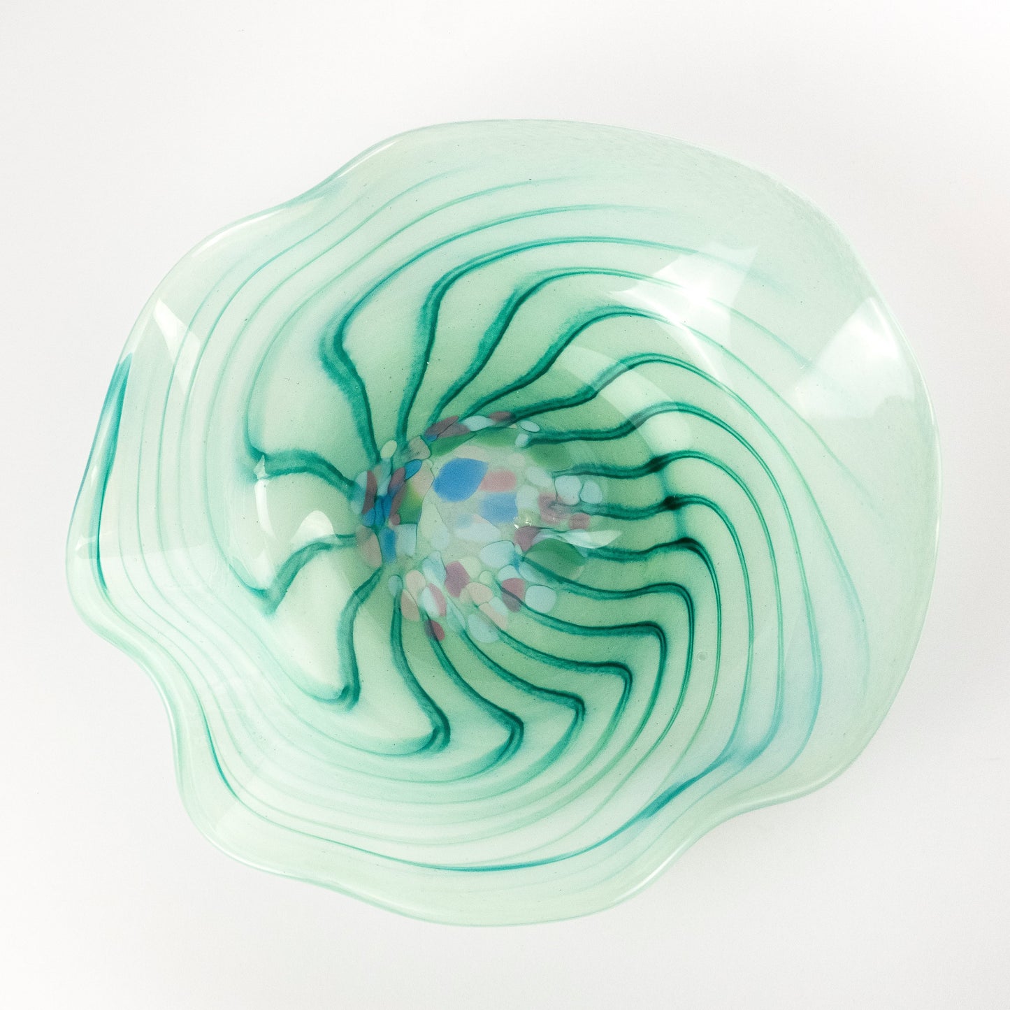 A hand-blown glass bowl with a wavy, scalloped rim, featuring a light mint green base with concentric teal-green swirls and a small multicolored center detail, set against a plain white background.