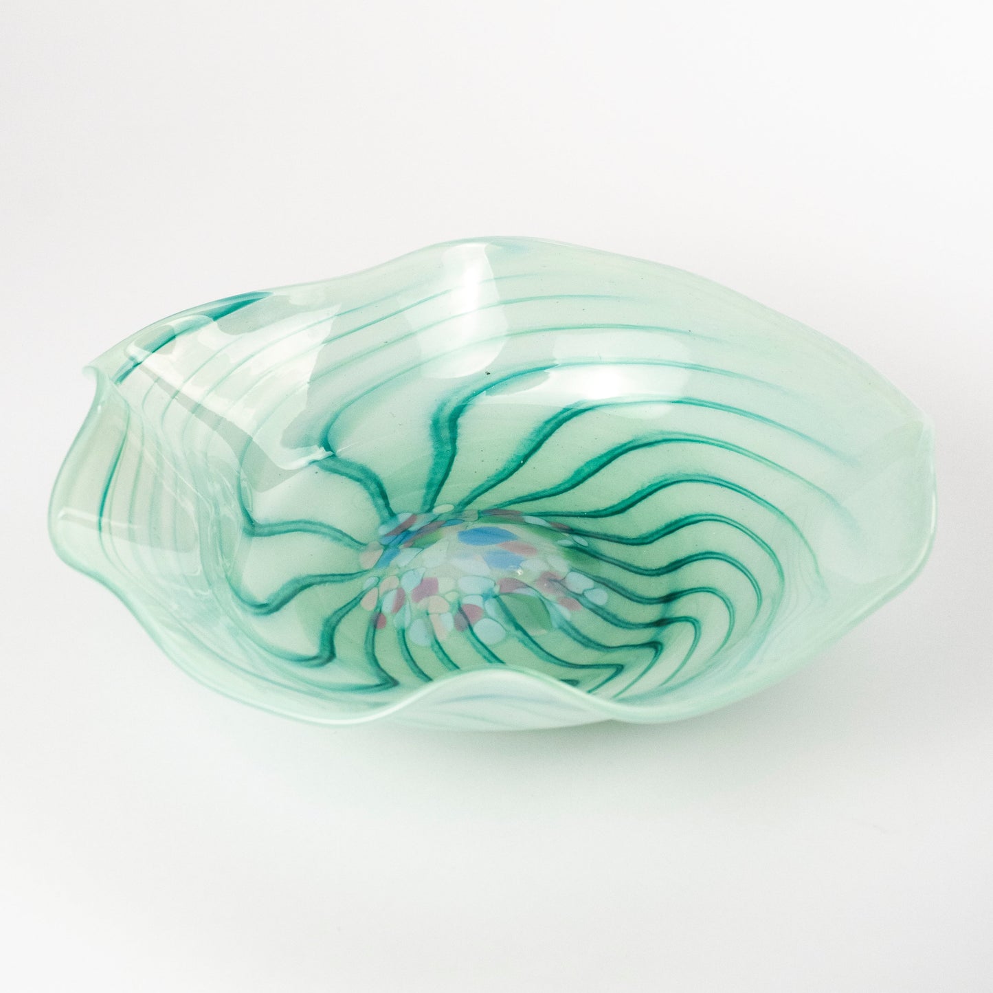 A hand-blown glass bowl with a wavy, organic shape, featuring a light mint green base with dark green swirling patterns and a small iridescent blue and pink center, set against a plain white background.