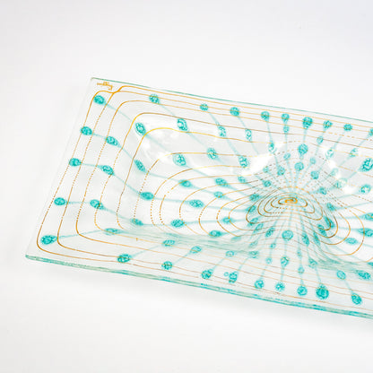 A clear glass rectangular platter with a raised rim, decorated with concentric gold lines and turquoise blue circular motifs, shown on a white background.