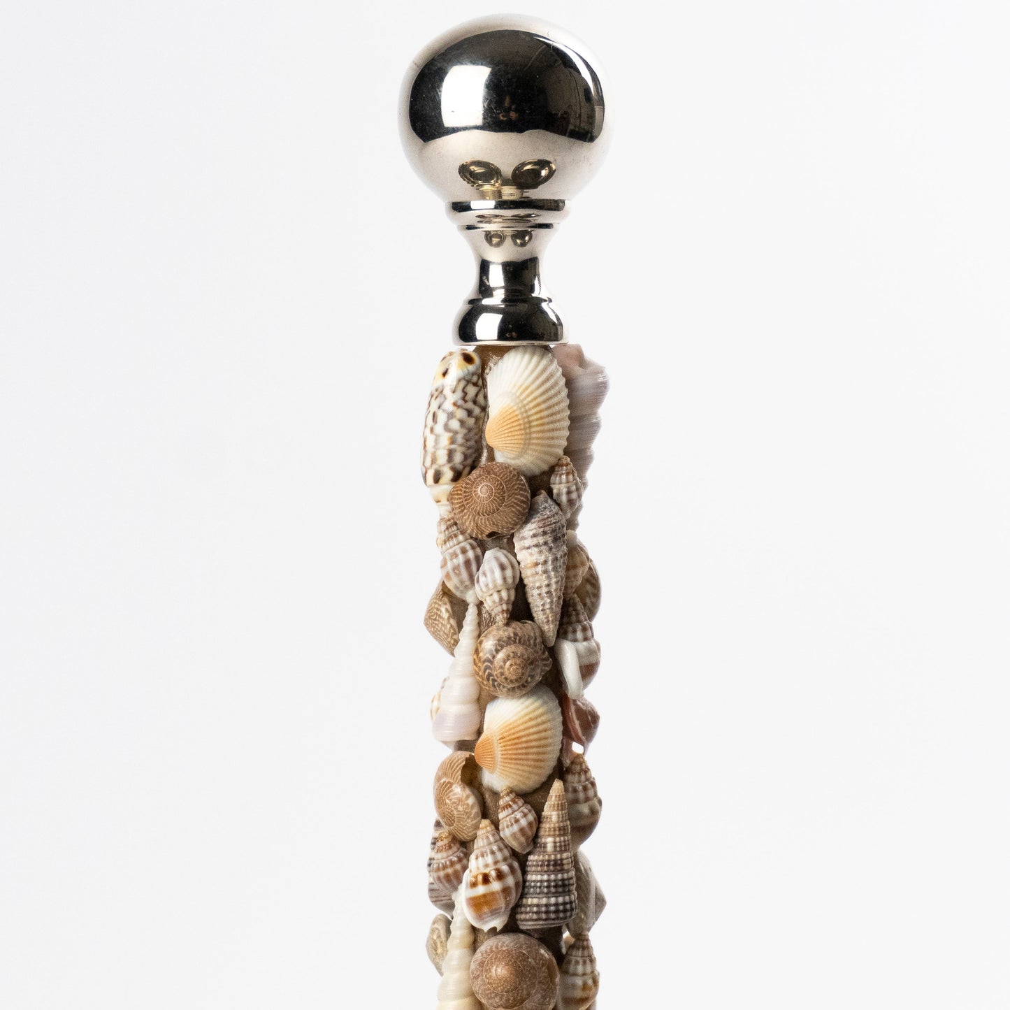 A decorative metal trio serving dish with a central handle covered in assorted seashells and topped with a polished metallic ball, shown against a clean white background.