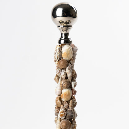 A decorative metal trio serving dish with a central handle covered in assorted seashells and topped with a polished metallic ball, shown against a clean white background.