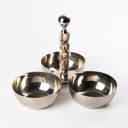 A polished silver-toned metal three-bowl serving stand with a central pillar designed with seashells, photographed on a clean white studio background.