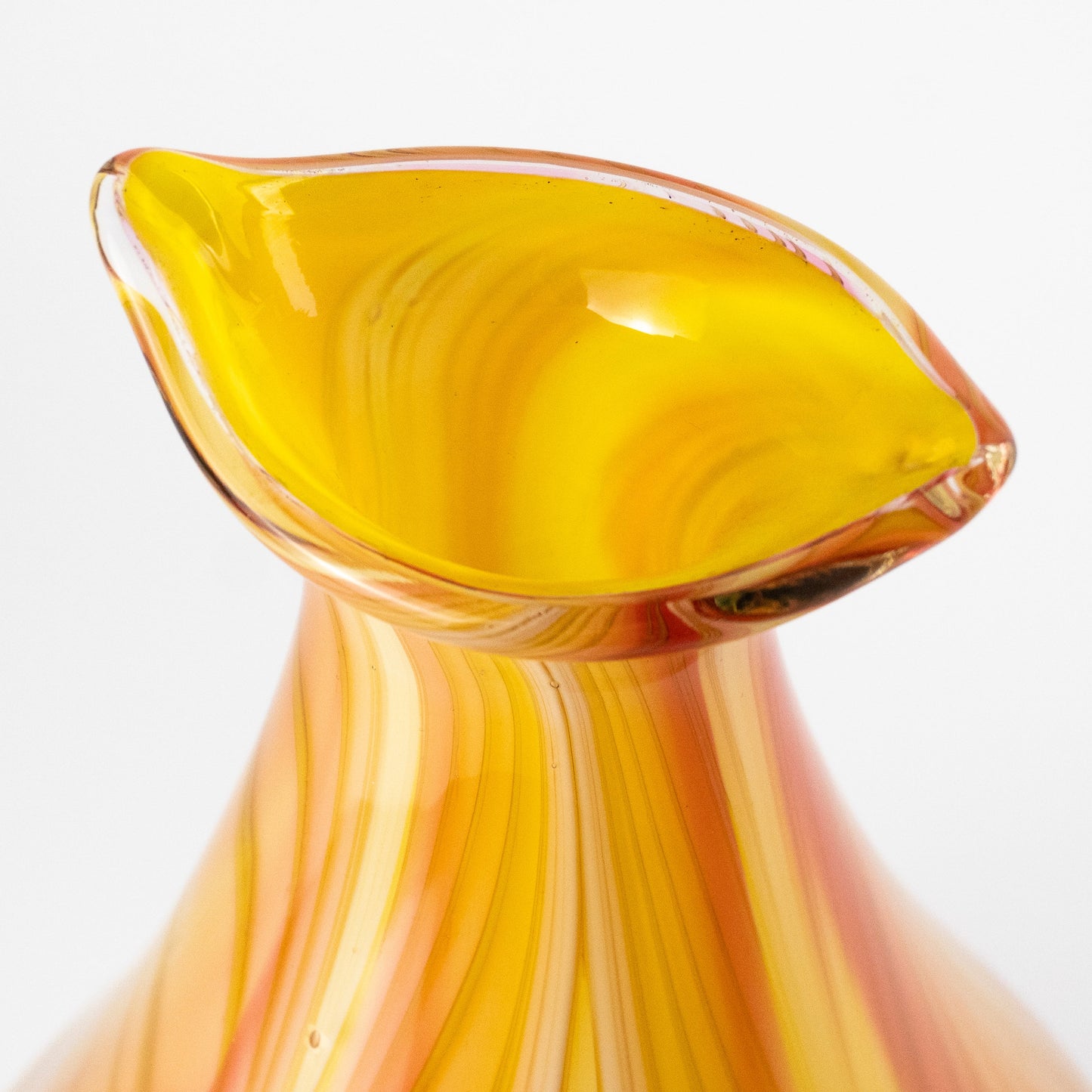 Close-up of a hand-blown glass vase with a flared rim, featuring vibrant yellow, orange, and peach swirls on a white background.