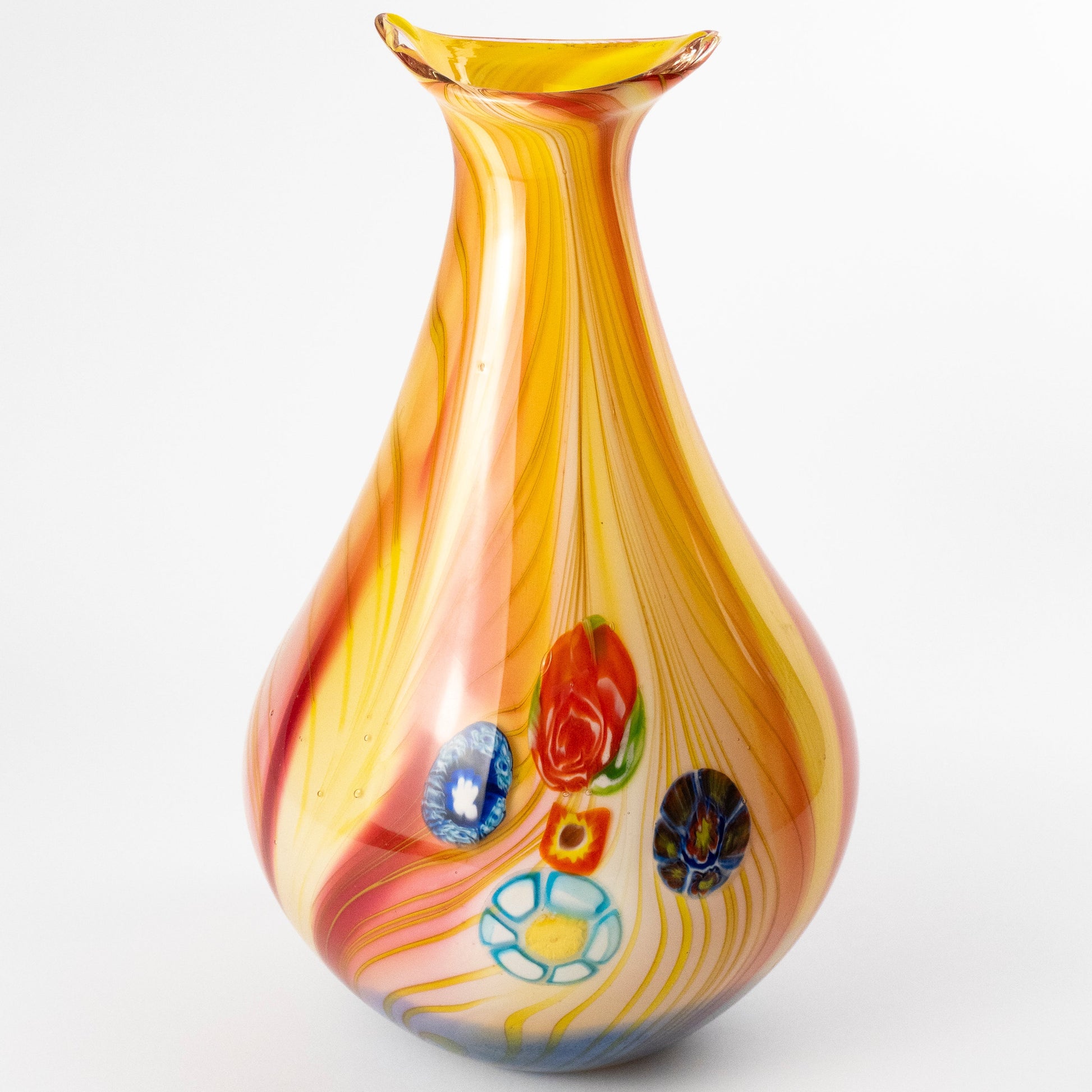 A hand-blown glass vase with a teardrop silhouette, featuring a yellow and orange marbled body with red, blue, and white decorative glass flowers, set against a plain white background.