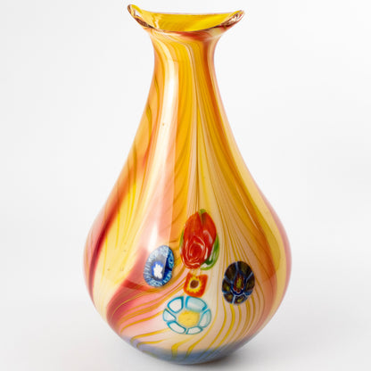 A hand-blown glass vase with a teardrop silhouette, featuring a yellow and orange marbled body with red, blue, and white decorative glass flowers, set against a plain white background.