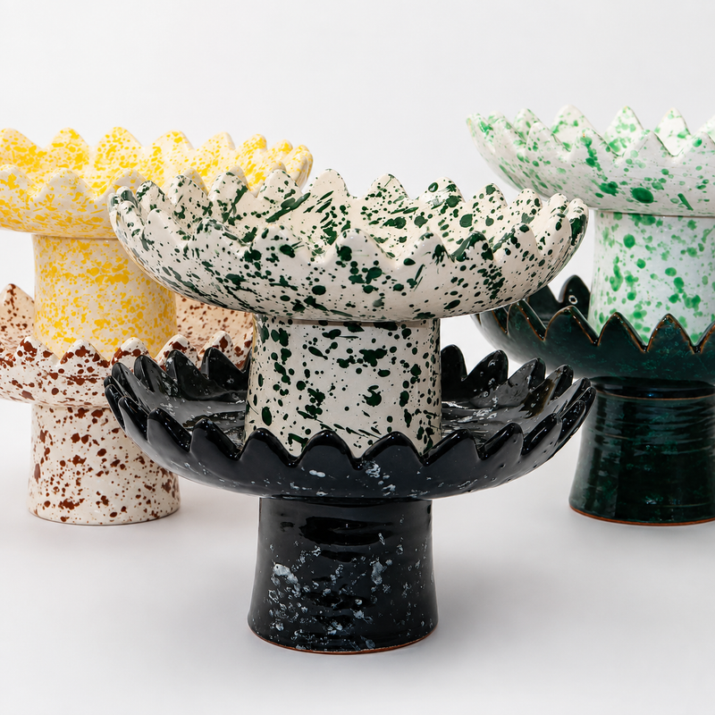Floree ceramic pedestal bowls in five colorways — yellow, brown, green, black, and deep green speckle — with sawtooth zigzag rims and footed bases
