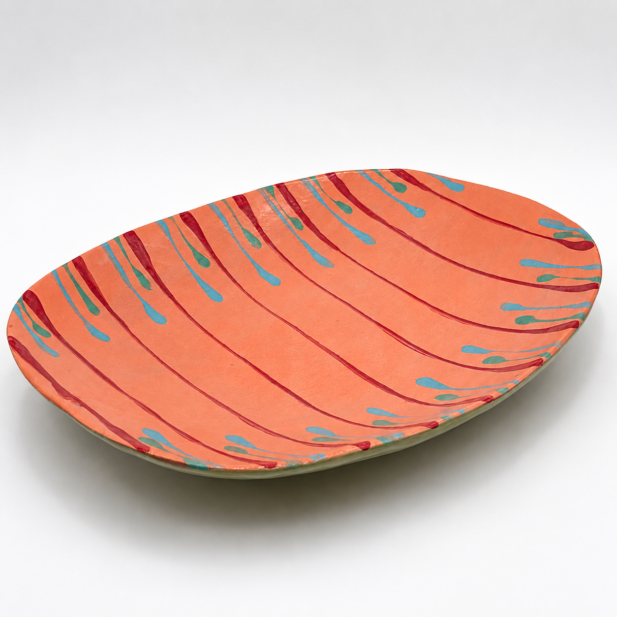 Tiera oven-safe ceramic serving bowl in coral with hand-painted magenta, teal, and blue drip pattern