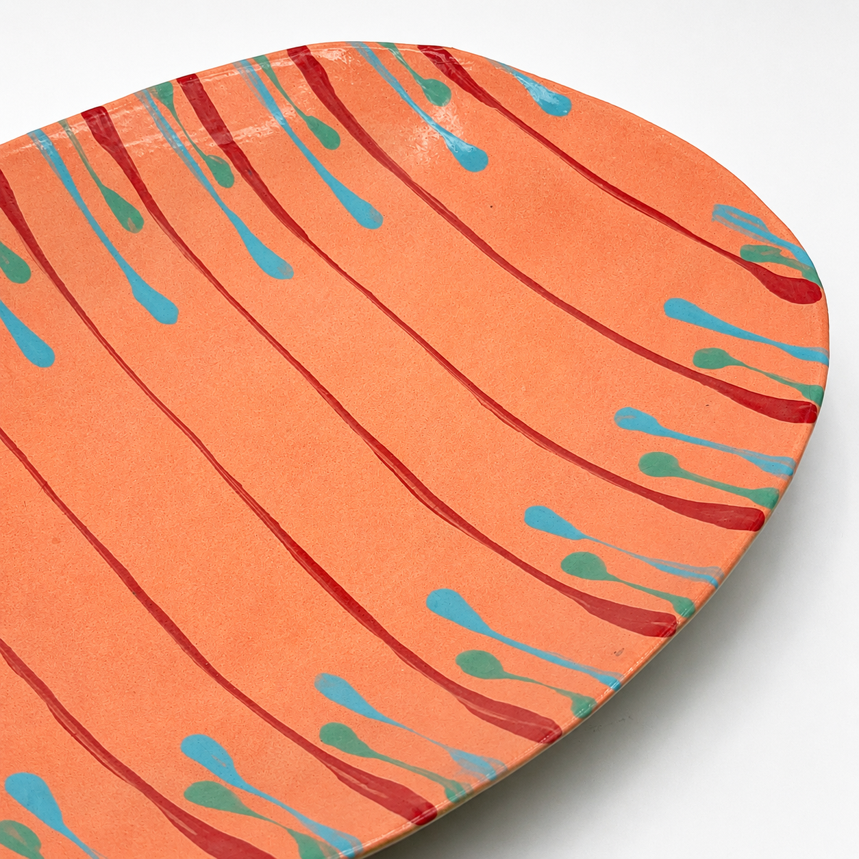 Detail view of Tiera oven-safe ceramic serving bowl showing colorful drip glaze pattern on coral base